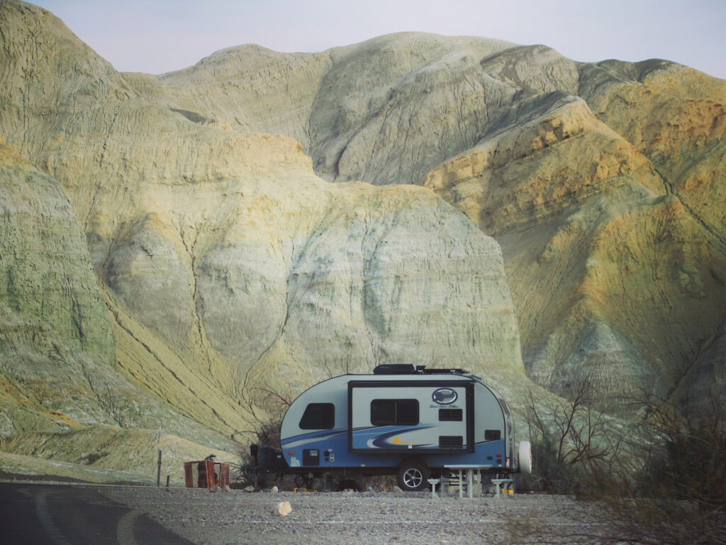 Blue and white trailer in front of massive beige and yellow cliff.