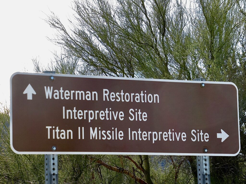 White lettering on brown sign reading: Waterman Restoration Interpretive Site Titan II Missile Interpretive Site with arrows pointing up and to right.