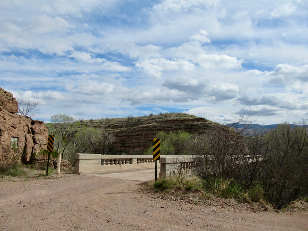 Concrete bridge with gravel road and low hills.
