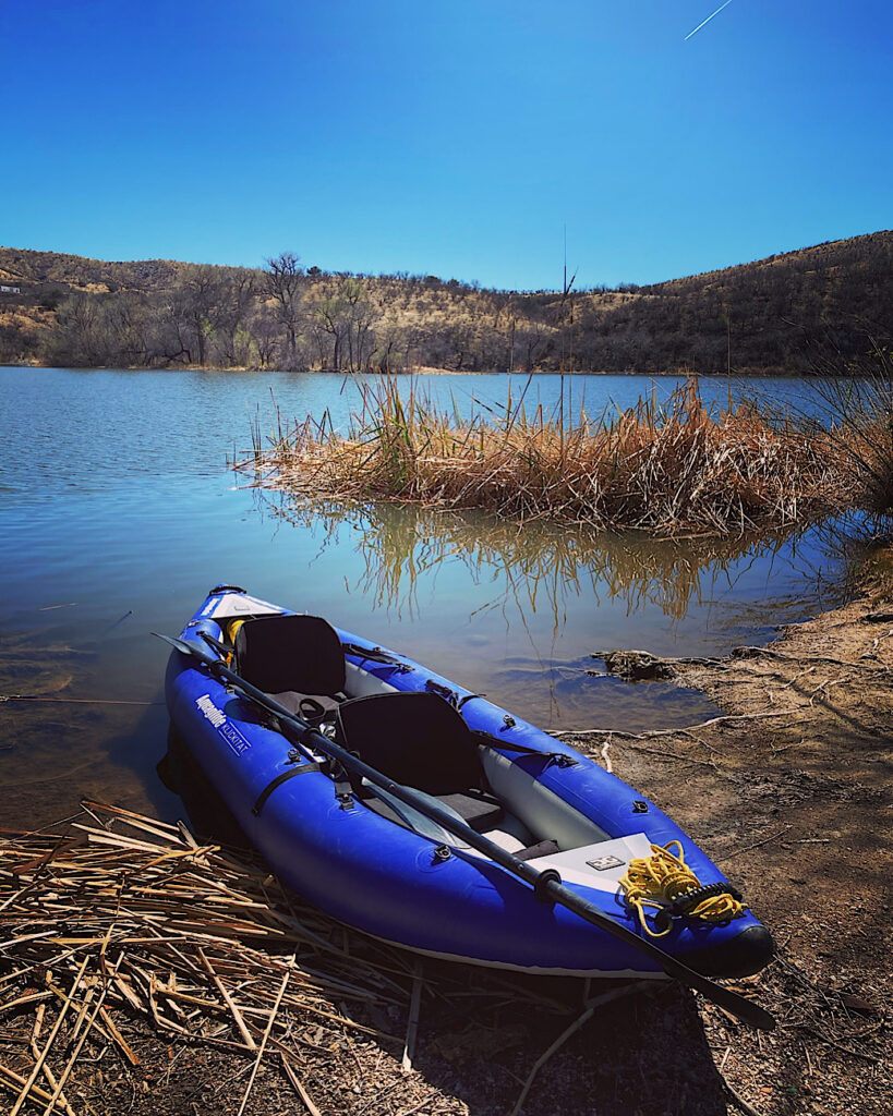 Blue inflatable double kayak pulled up lakeside.