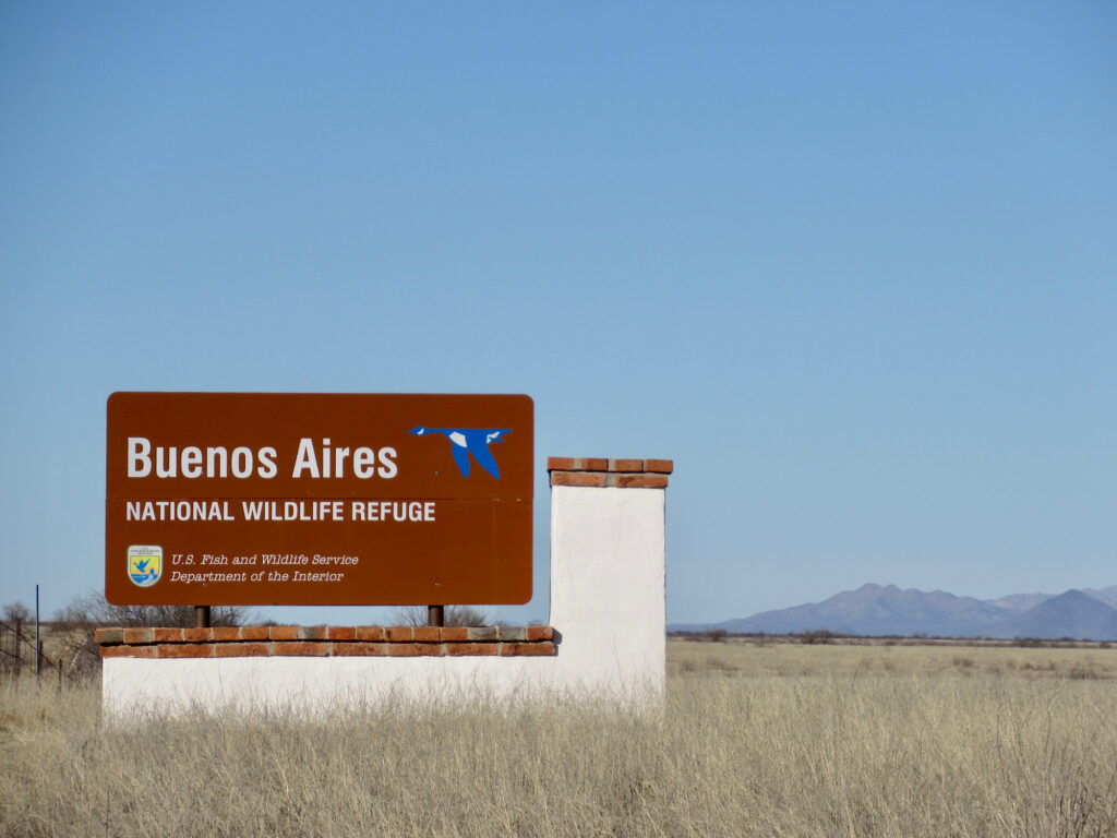 Brown sign on white base topped with brick. Sign had blue and white goose image and reads: Buenos Aires National Wildlife Refuge. U.S. Fish and Wildlife Service Department of the Interior.