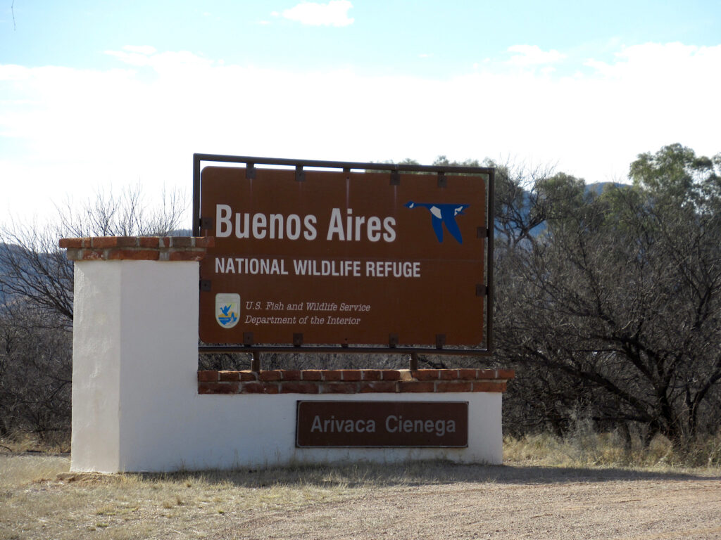 Brown entrance sign on white base reading: Buenos Aires National Wildlife Refuge Arivaca Cienega.