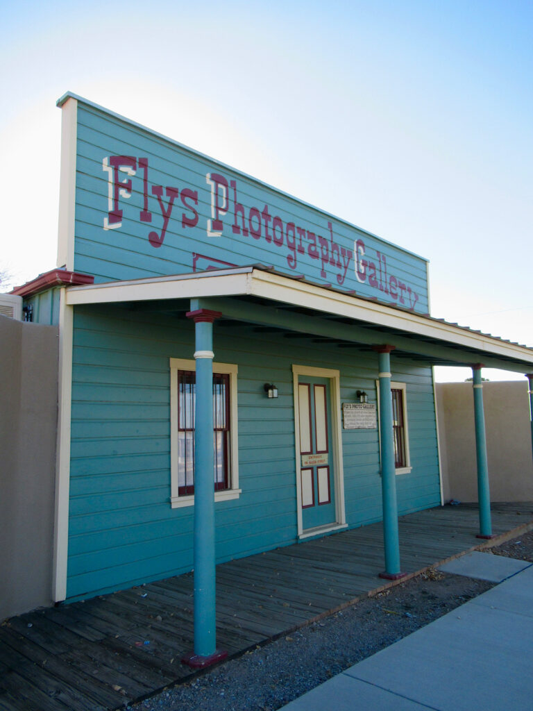 False front western-style building painted turquoise with cream accents. Flys Photographic Gallery written across top of the building.