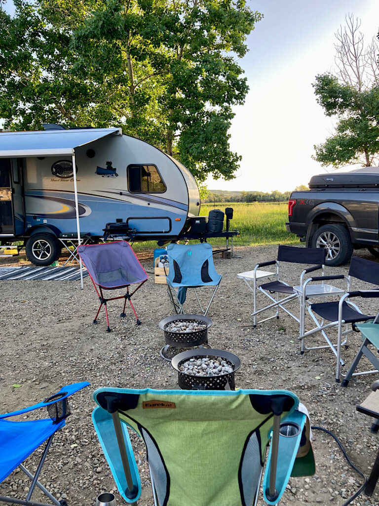 Miscellaneous group of camping chairs set up around two portable fire-it's in a campsite with truck and trailer.