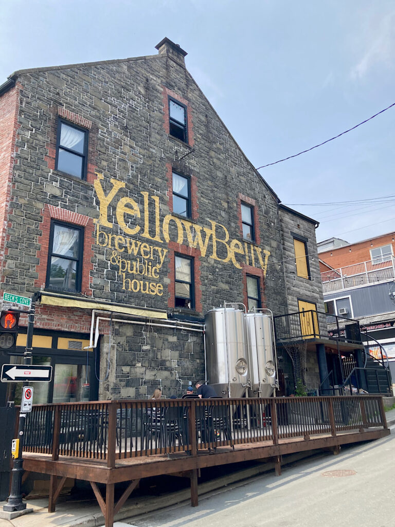 Historic stone building with two large silver tanks on patio and Yellowbelly Brewery and Public House written in yellow on the side.