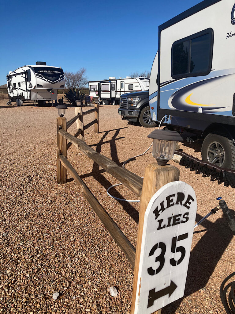 Split-rail log fence with black and white sign at one end reading: "Here lies 35" to mark RV camping spot.