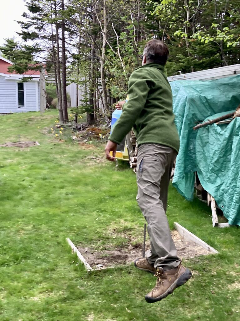 Man in brown pants and green jacket playing horseshoes.