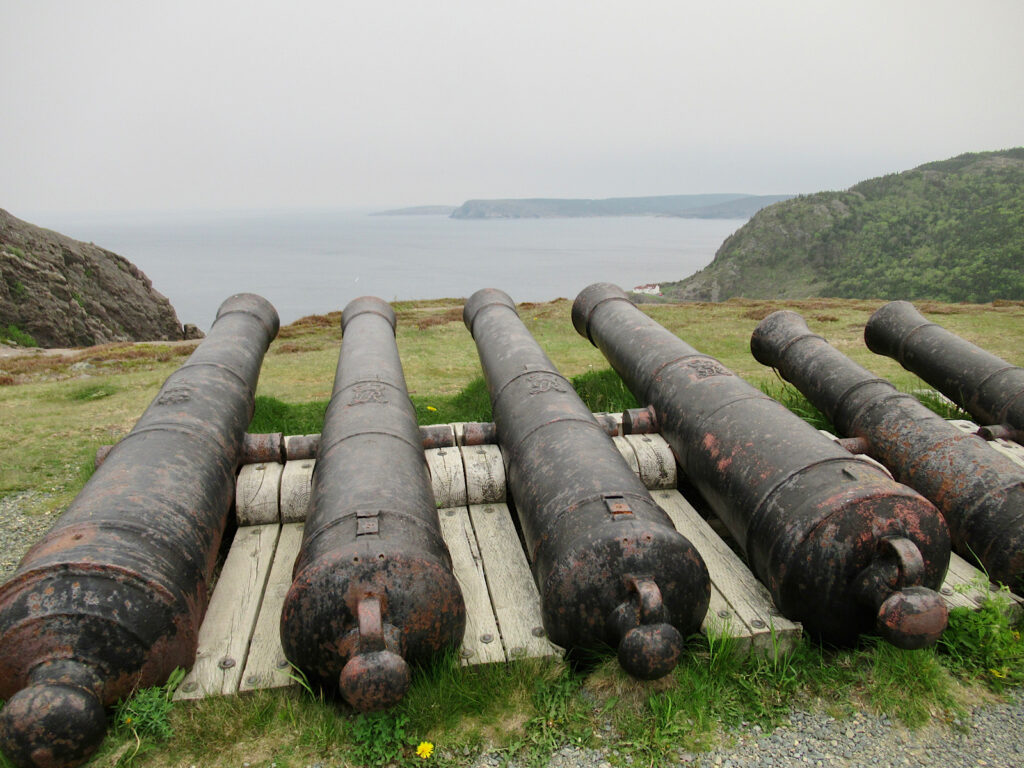 Six gun barrels lined up on cliff overlooking the ocean.