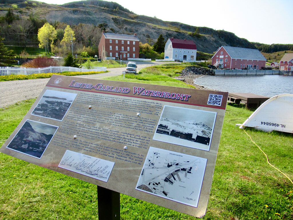 Interpretive sign in foreground with historic buildings in background beside ocean.
