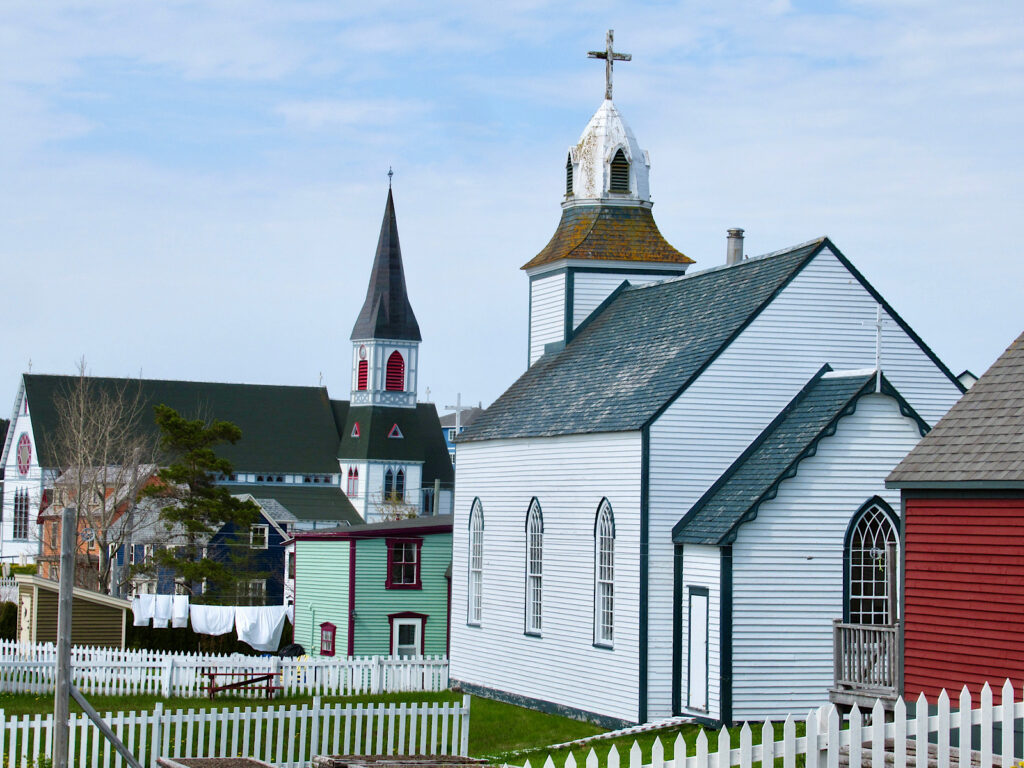 Historic white church with colourful building in background.
