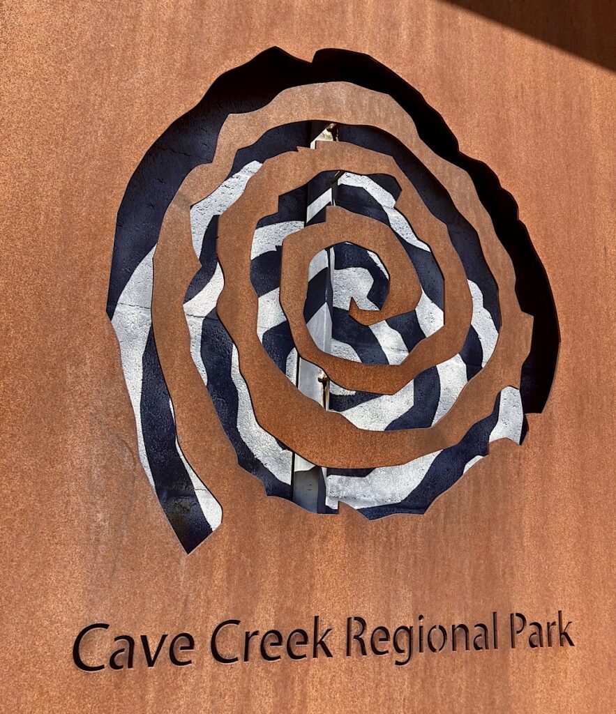 Metal sign with cut out spiral petroglyph symbol and words: Cave Creek Regional Park