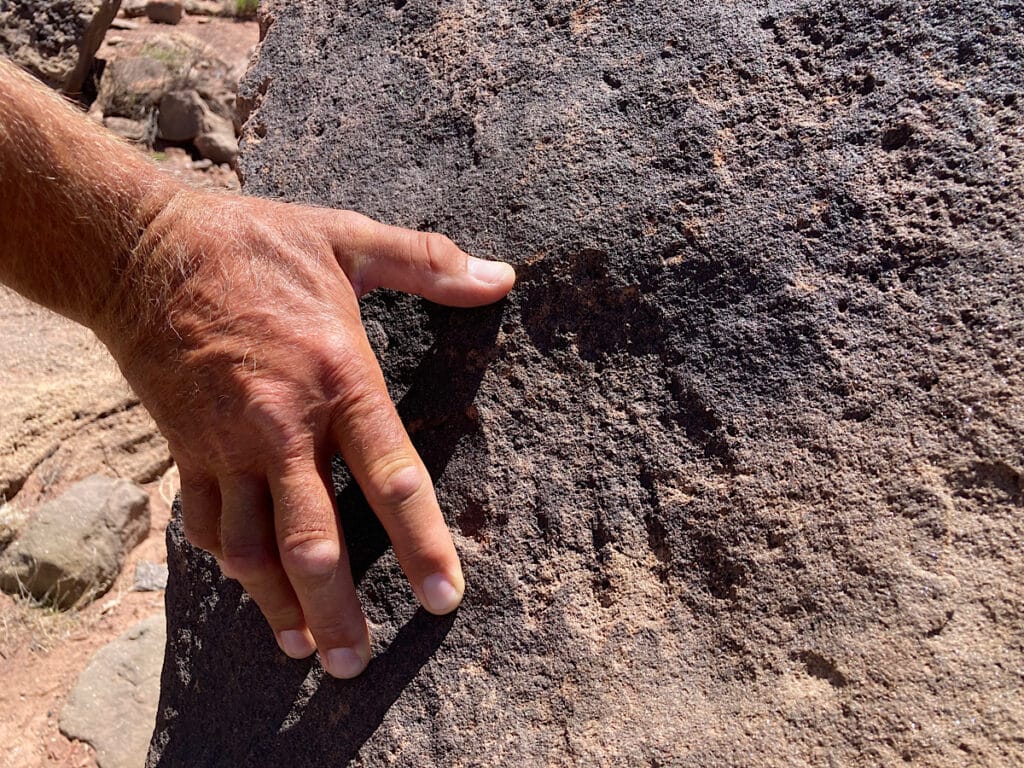 Tiny handprint carved into rock with man's hand beside for scale.