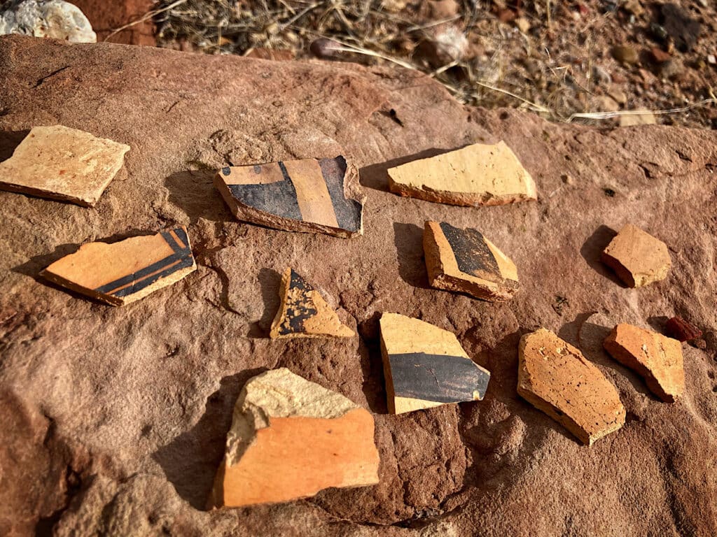 A collection of pottery sherds - many with black paint markings - on reddish coloured rock.