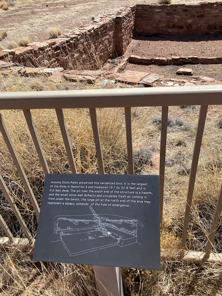 Interpretive panel discussing facts about the reconstructed stone walls beyond metal fence.
