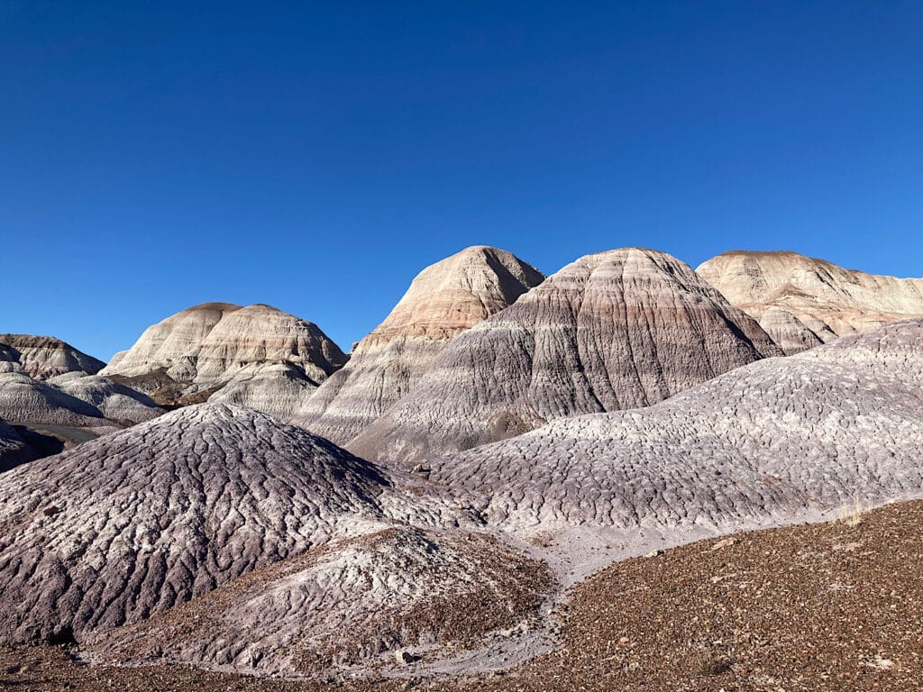 Photo of badland-type hills in shades of mauve, blue and grey under deep blue sky.