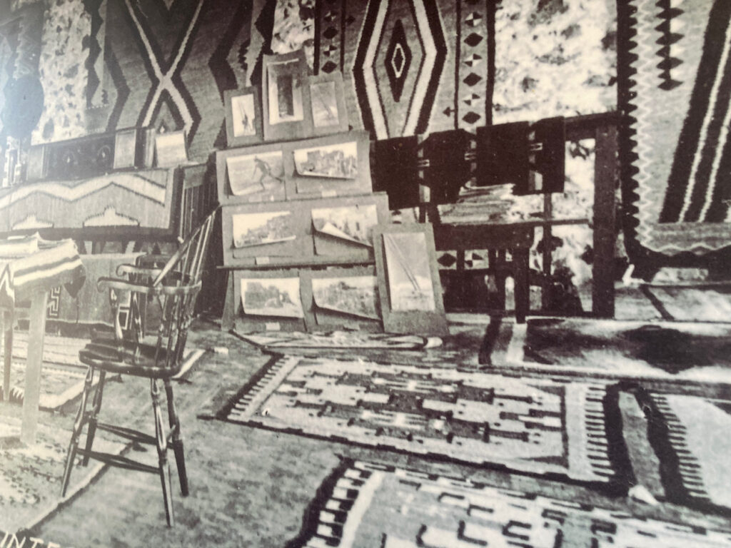 Black and white photo of a room with a single wooden chair and Native American rugs on walls and floor.
