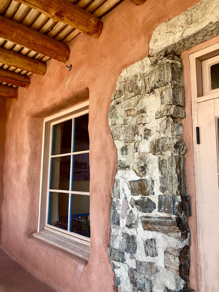 Red adobe building with petrified wood and mortar exposed next to edge of a white wood door.