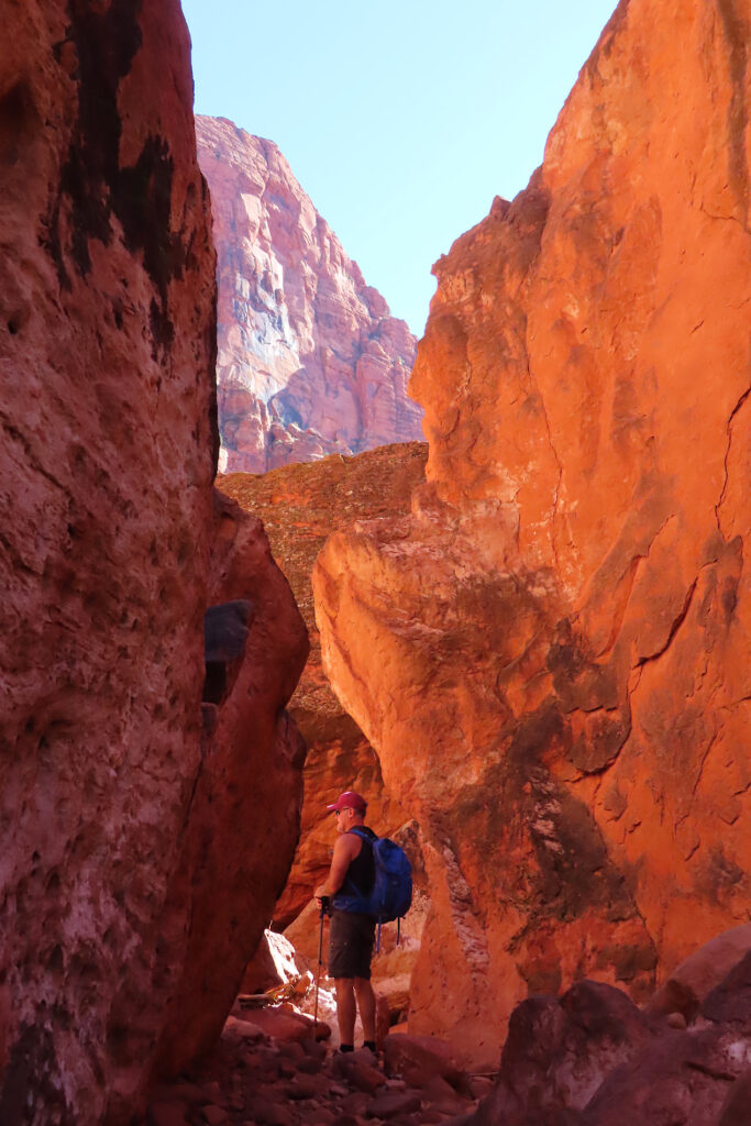 Man silhouetted in bottom glowing red canyon with a small patch of blue sky overhead.