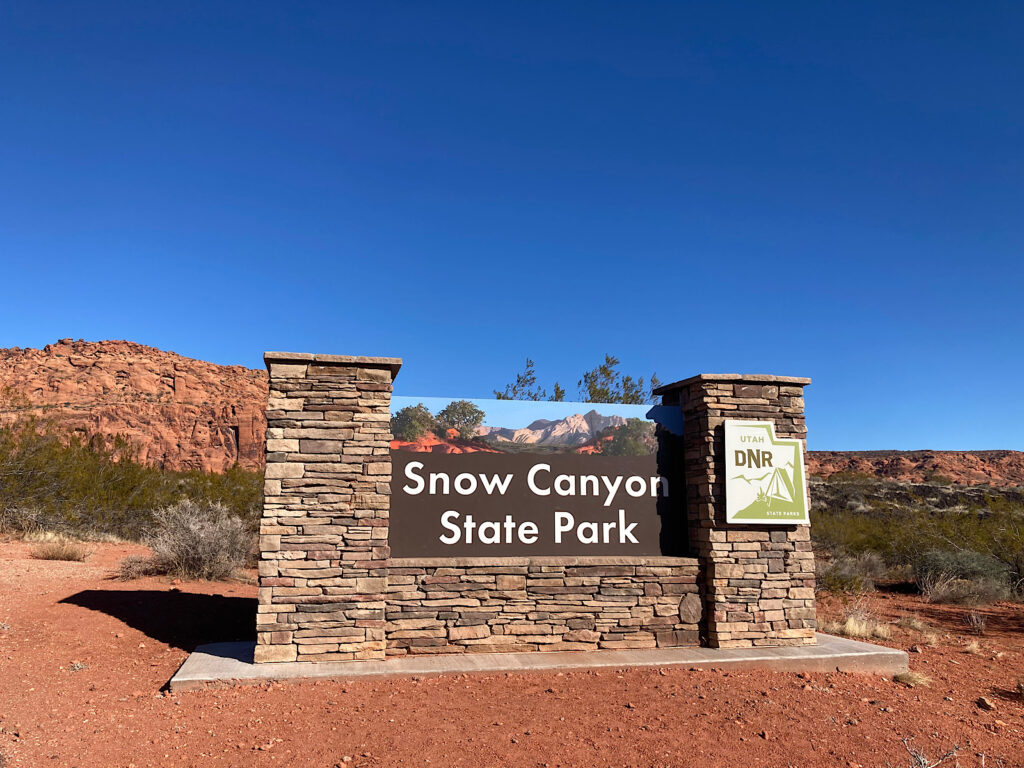 Wood and rock entrance sign to Snow Canyon State Park under blue sky.