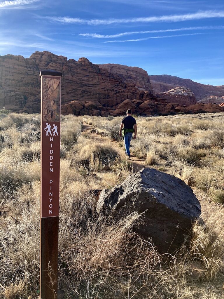 Man walking on trail with sign marking Hidden Pinyon trail.