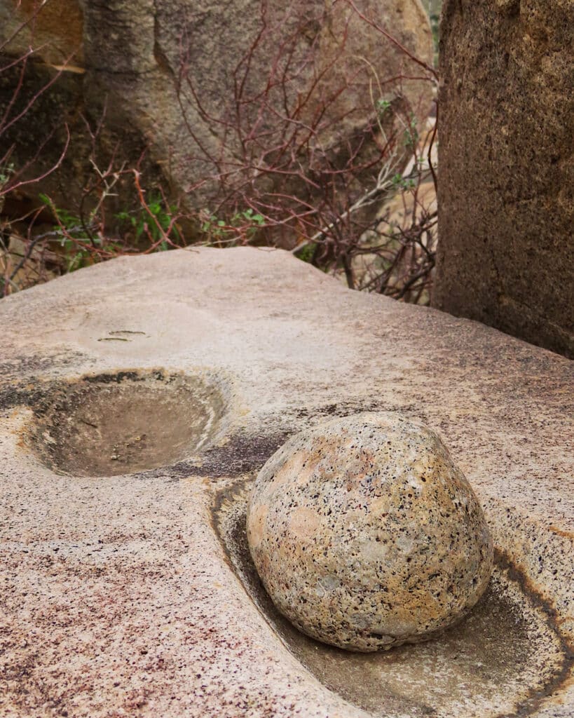 Round rock sitting in a depression on a pinkish brown granite boulder. 