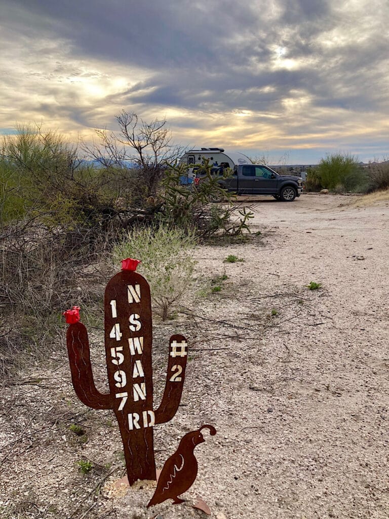 Metal cactus street address marker with truck and trailer parked in background.