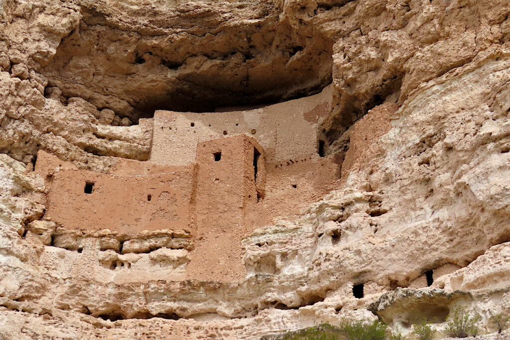 Multi-level red rock building built into rocky alcove.