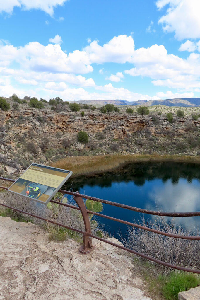 Interpretive sign on metal railing above deep blue pool surrounded by rocky ledge.