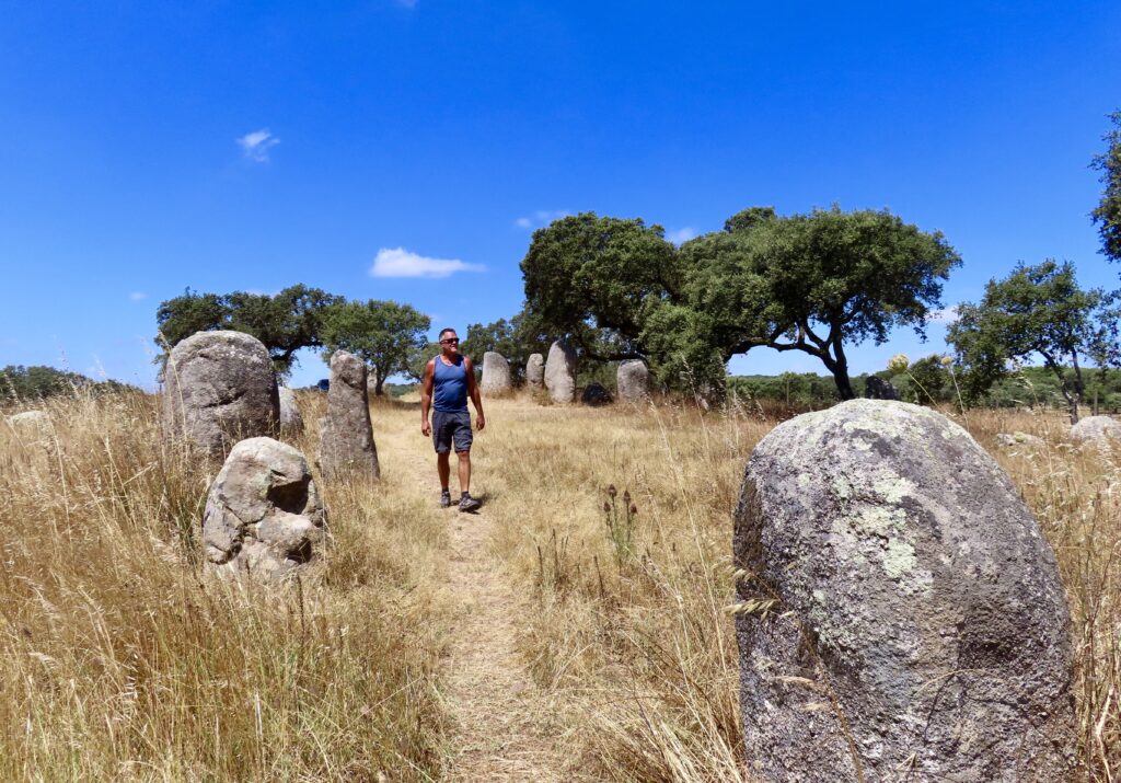 Man walking in dry grassy field dotted with large grey stones.