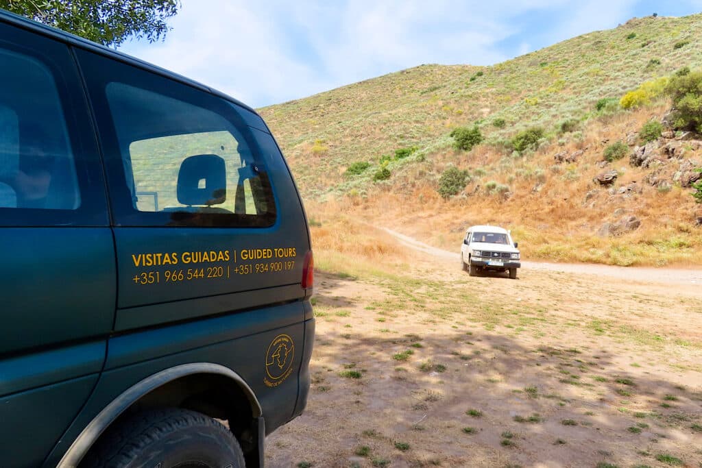 White 4x4 pulling into shade in front of a dry hill along with green van.