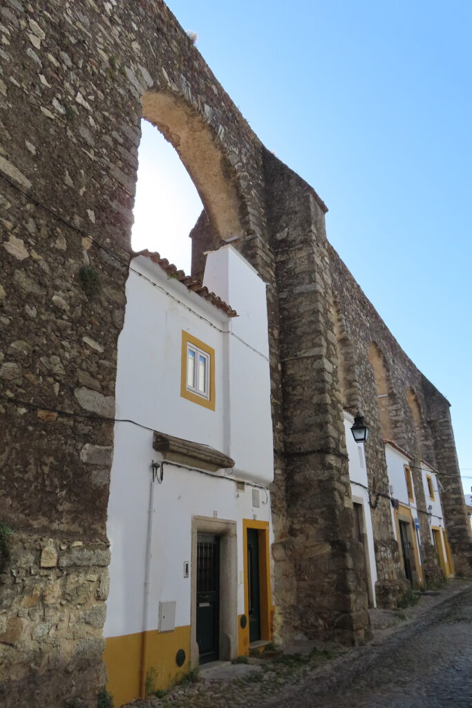 Stone arched wall with small whitewashed buildings built into the pillars.