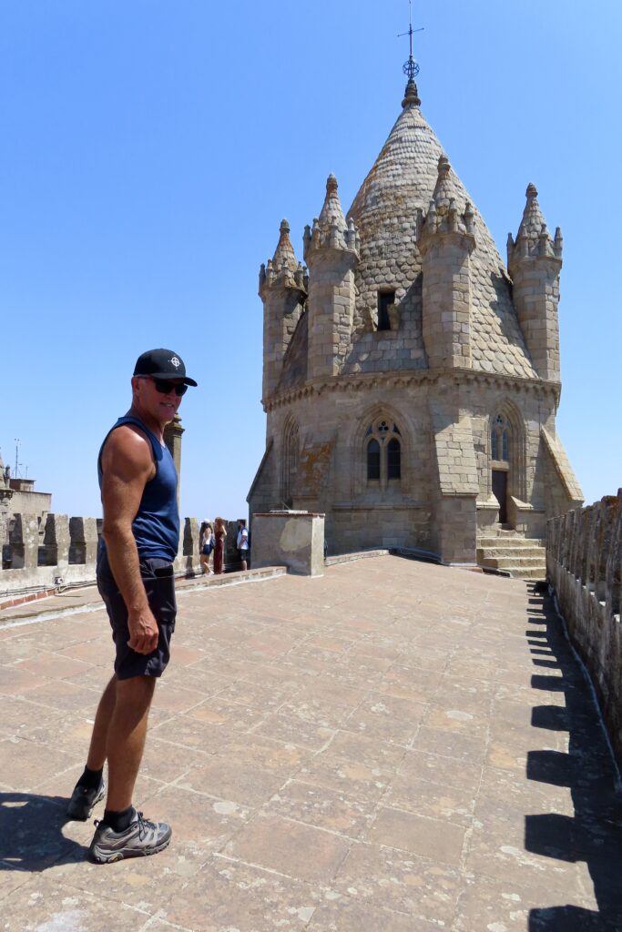 Man in shorts and short sleeve top up on roof of a building with elaborate rooftop structure behind him.