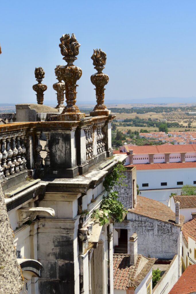 View of red-roofed, white-washed buildings and countryside from rooftop with elaborate stone wall.