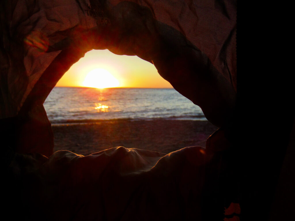 Sunrise view out of tent overlooking water and beach.