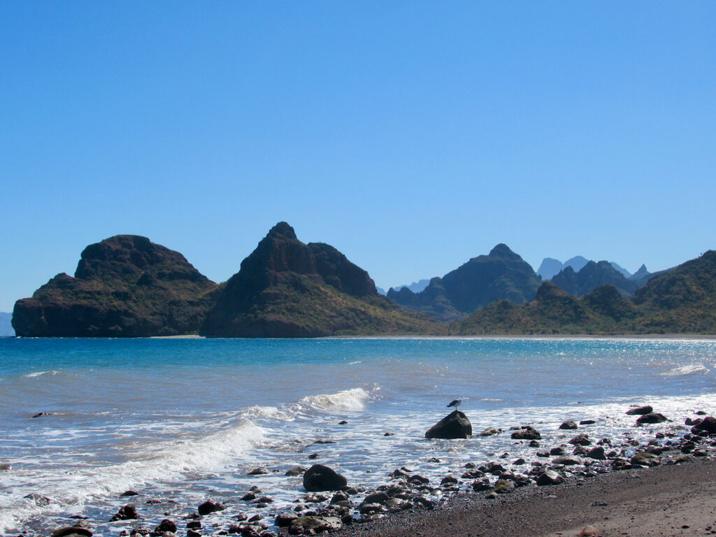 Rugged mountains and blue water foaming white near rocky beach.