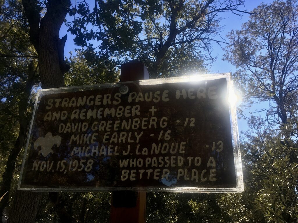 Backlit sign with words: Strangers pause here and remember David Greenberg - 12, Mike Early - 16, Michael J. LaNoue - 13 who passed to a better place. November 15, 1958.