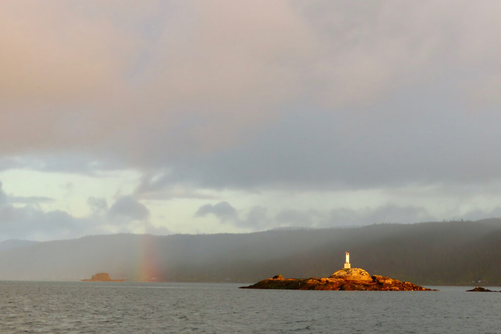 Distant rainbow over open water with small light on island.