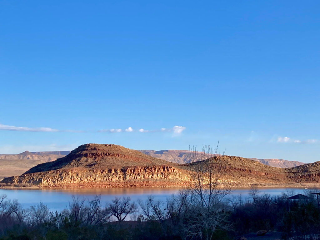 Multi-coloured rocky hills across lake under blue sky.