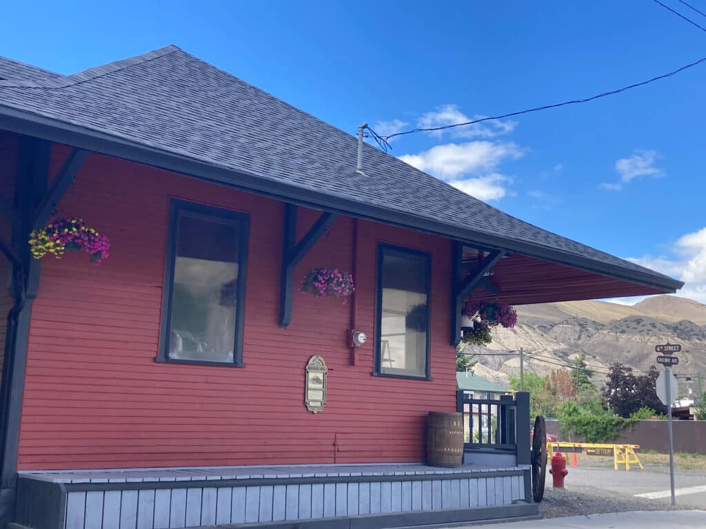 Red building with grey roof on street corner under blue sky.