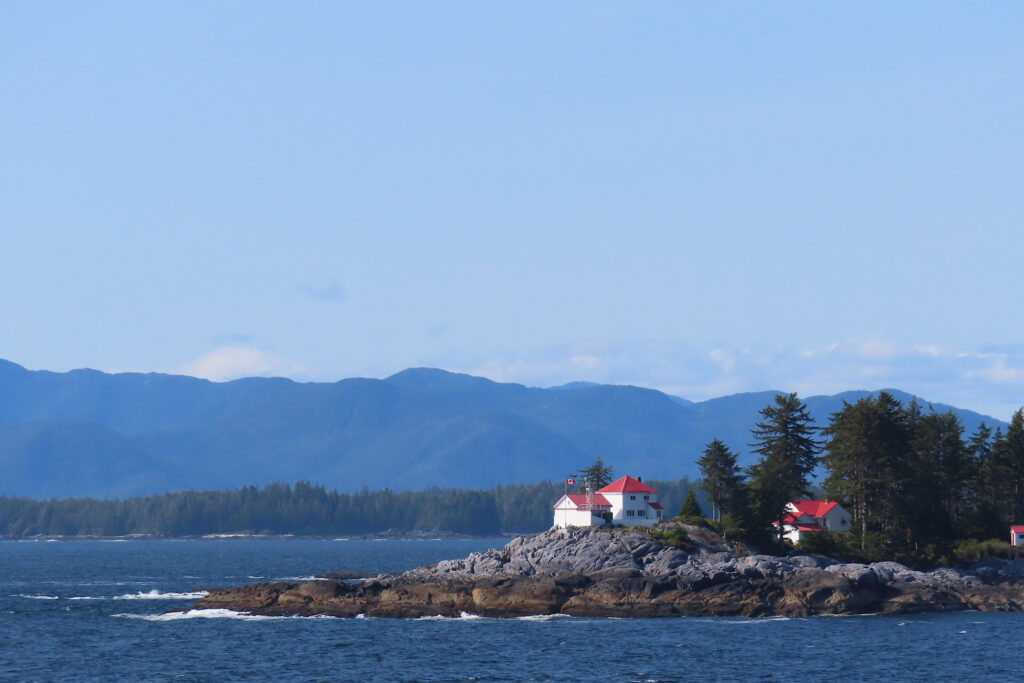 Small lighthouse on ocean island with distant mountains.