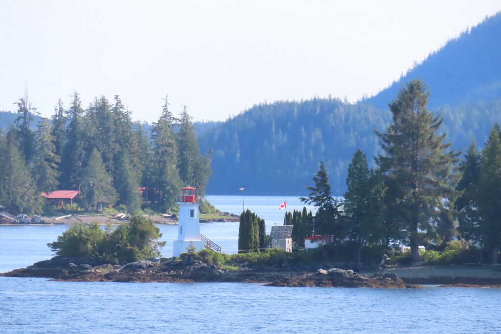 Lighthouse on narrow point of land in front surrounded by water.