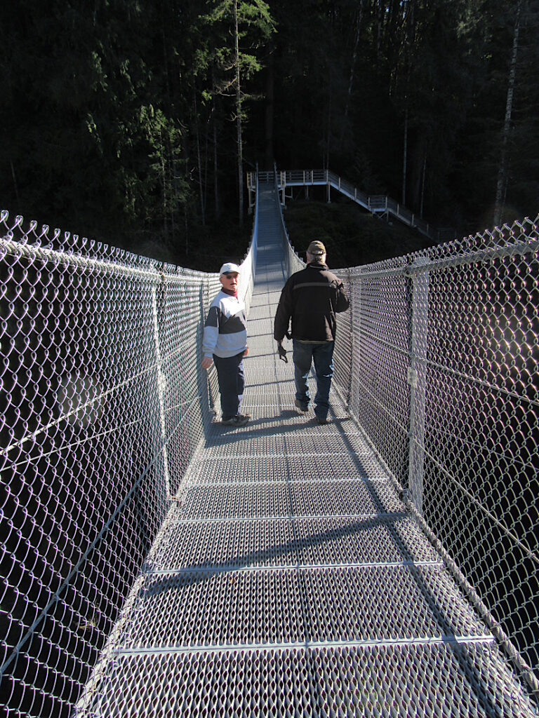Two men walking on metal and wire suspension bridge.