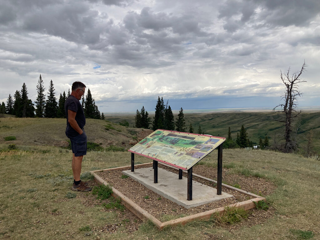 Man stand in front of interpretive panel on edge of a ravine.
