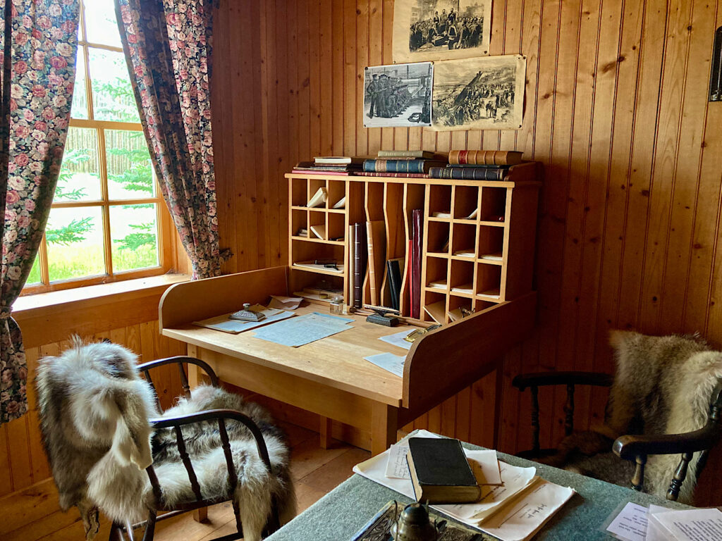 Interior of historic building furnished with wood desk and chair covered with furs.