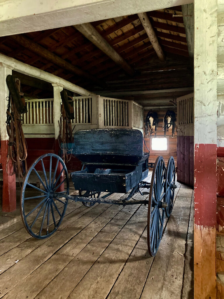Interior of a stable with stalls and a black carriage.