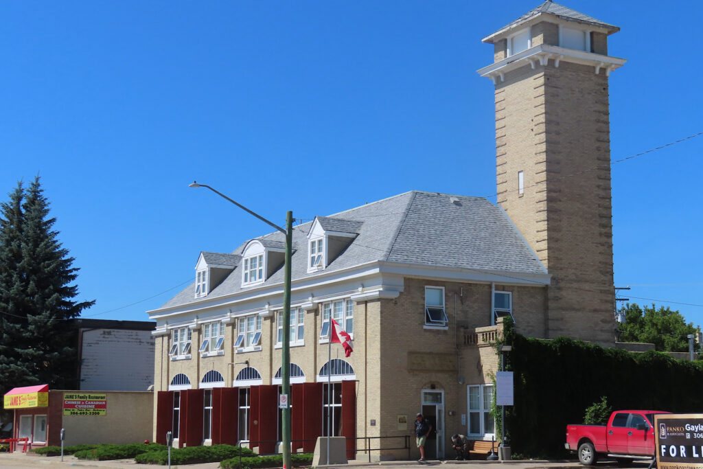 Brick building with mulitiple entrances and tall tower at back.