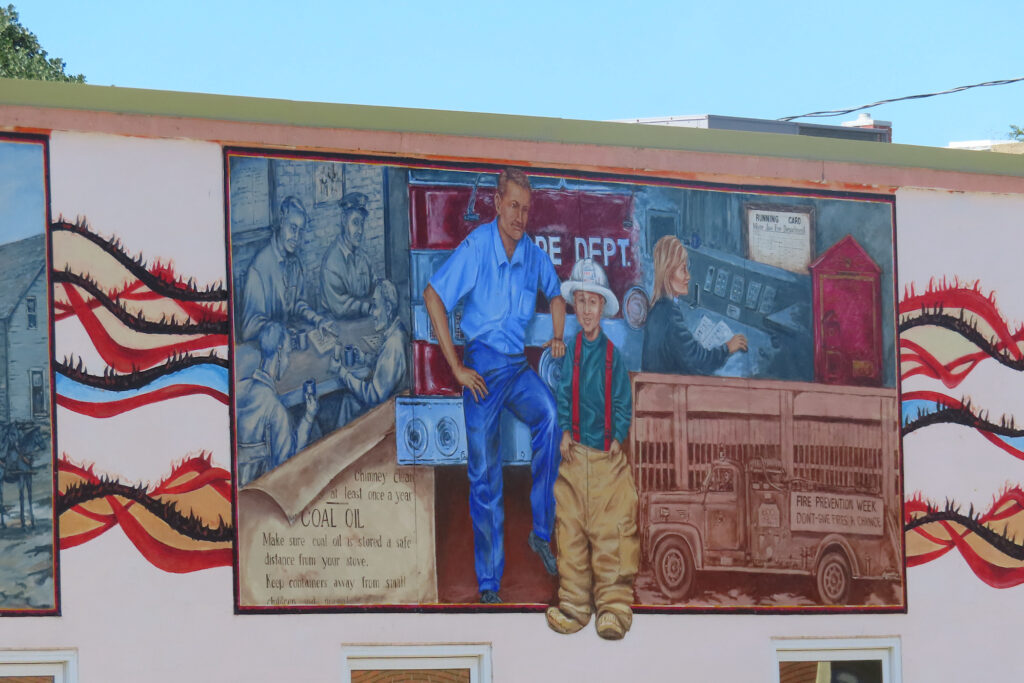 Painting on a young boy dressed in firefighting clothing beside a firefighter in uniform.