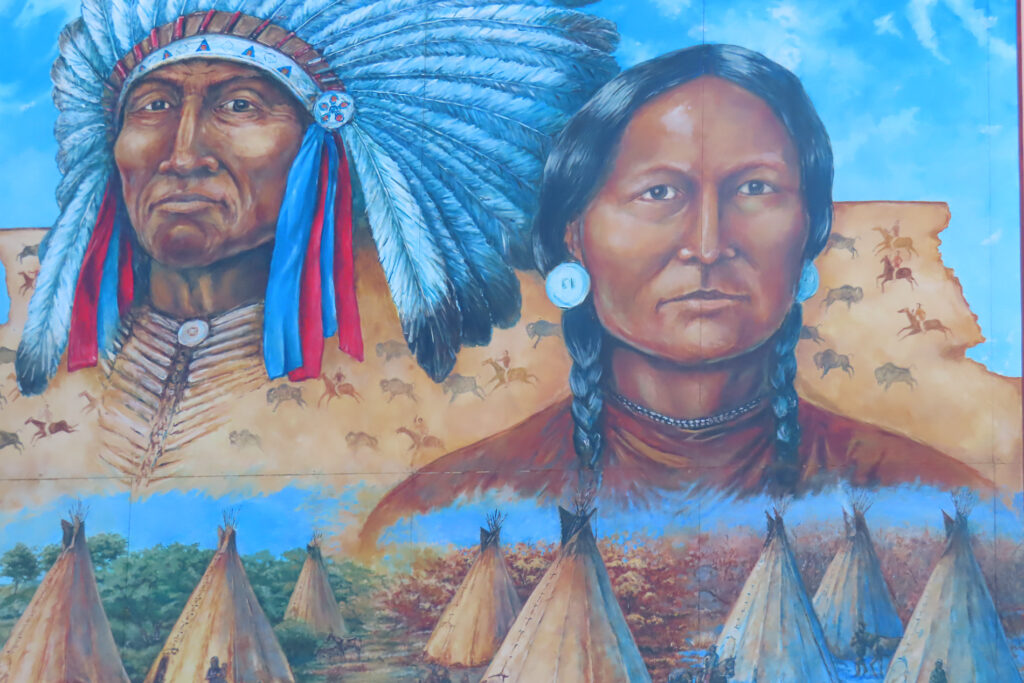 Painting for First Nations in headdress and teepees below.