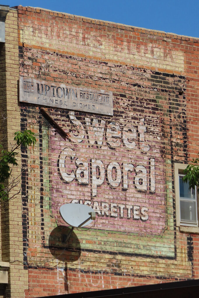 Old painted layers of advertisements on side of red brick buiilding.