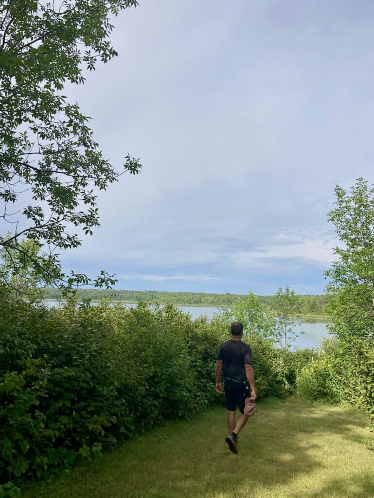 Man walking grassy trail towards a lake.